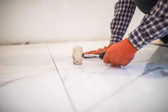 Person verlegt Fliesen mit Gummihammer